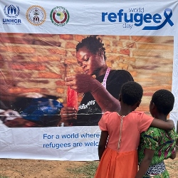 This picture was captured on World Refugee Day (20th June 2024) in Ukende Refugee Settlement, Ogoja, Nigeria.       "A pair of youthful refugee friends enthralled with a seamstress featured on a world refugee day poster. The children help one another read