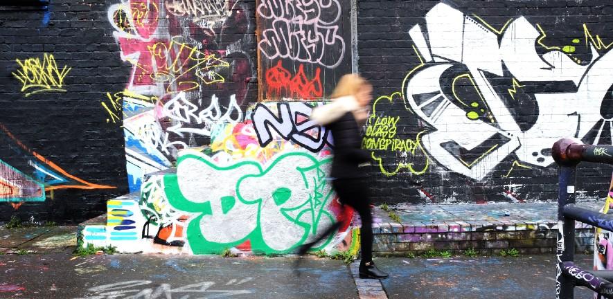 Women walks past bright blue graffitti on a housing estate in Manchester