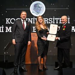 Professor Ayse Zarakol in black dress being awarded the Rahmi M. Koç Medal of Science certificate with two formally dressed presenters